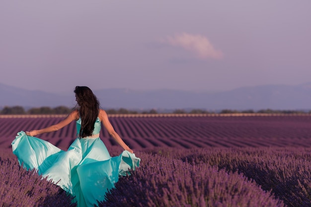 Champ de fleurs de lavande femme en robe cyan s'amusant et se détendant sur le vent dans un champ de fleurs violettes