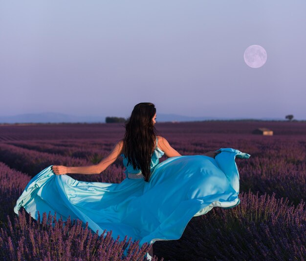 Champ de fleurs de lavande femme en robe cyan s'amusant et se détendant sur le vent dans un champ de fleurs violettes