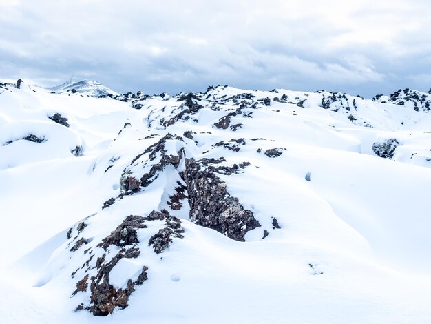 Champ de neige avec des montagnes sous un ciel nuageux en Islande