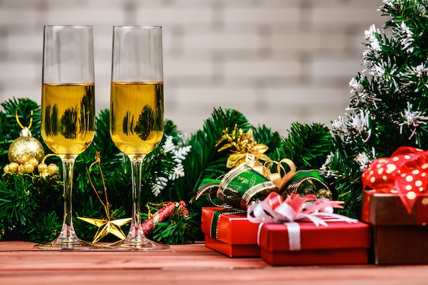 Champagen deux verres à côté de coffrets cadeaux rouges et or, un petit pin artificiel, des décorations de noël, préparez-vous pour célébrer la planche de bois, fond flou de mur de briques blanches.