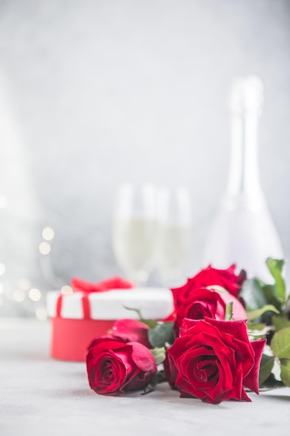 Champagne et roses rouges avec bokeh. Cadre de la Saint-Valentin avec roses rouges et cadeau