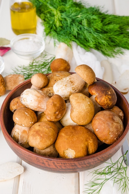 Champignons blancs des bois frais dans un bol avec des épices et des herbes fraîches sur bois