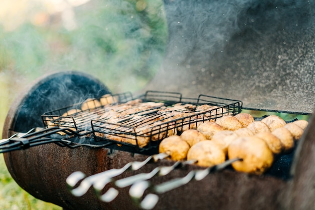 Les champignons en brochettes sont frits sur un barbecue au charbon de bois avec de la viande et des champignons frits sur le gril