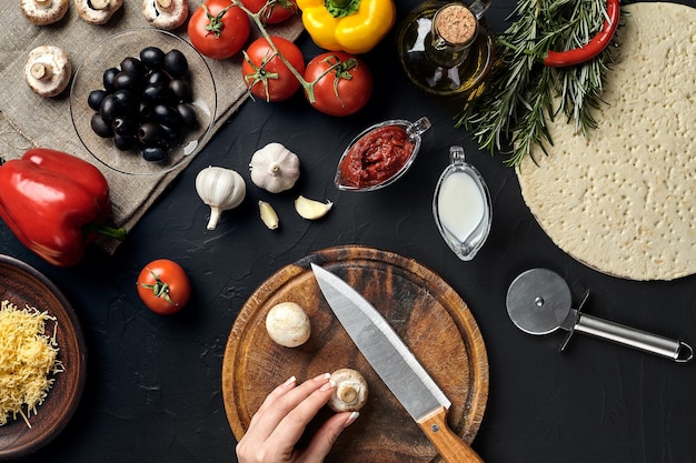 Champignons coupés à la main par une femme sur une planche de bois sur une table de cuisine autour de mensonge ingrédients pour pizza légumes fromage et épices