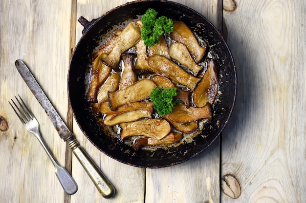 Champignons eringi frits dans une poêle sur une surface en bois