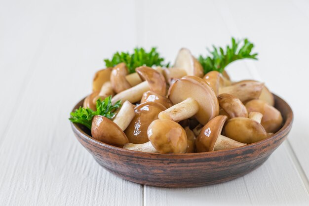 Champignons forestiers frais avec des verts dans un bol sur une table en bois.