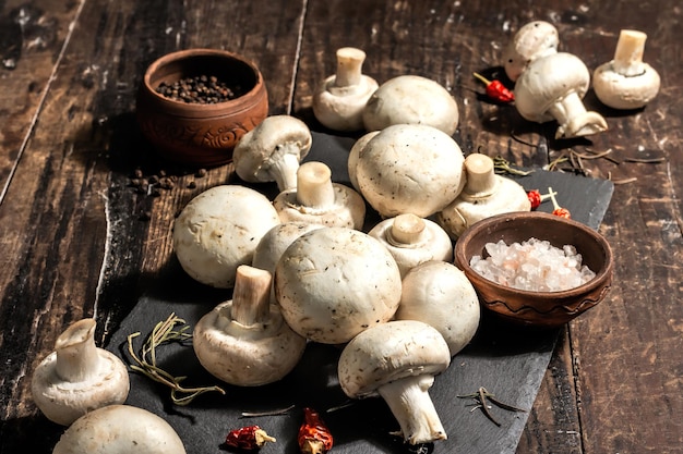 Champignons frais aux épices et herbes. Ingrédient cru pour la cuisson des aliments végétaliens. Vieux fond en bois, mode lumière dure, ombre sombre, style rustique, espace de copie