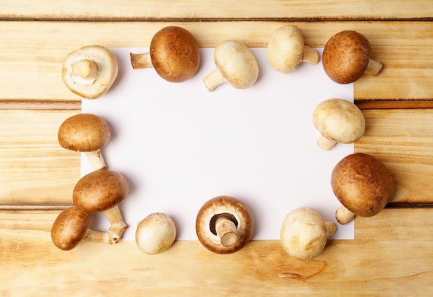 Champignons frais et feuille blanche vide sur fond en bois.