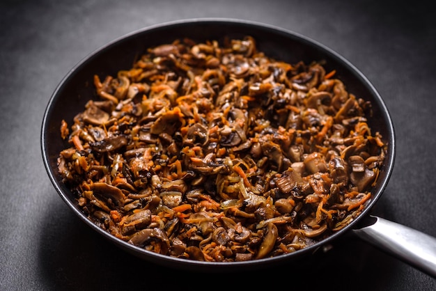 Champignons frits aux carottes oignons et épices dans une casserole sur un fond de béton foncé