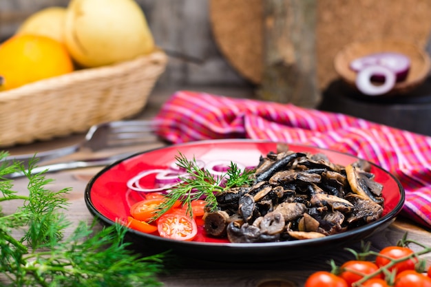 Champignons frits, oignons et tomates cerises sur une assiette sur une table en bois