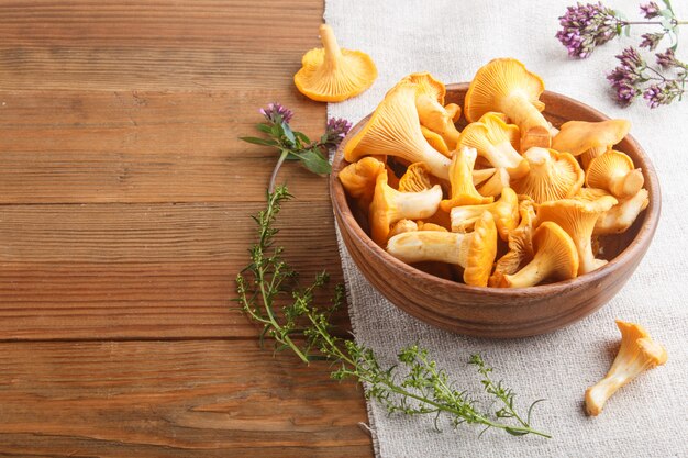 Champignons de girolles dans un bol en bois et herbes aromatiques avec textile en lin, vue latérale.