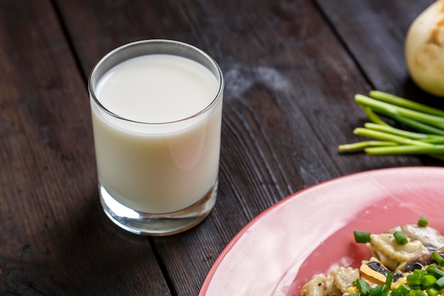 Champignons de lait et oignons verts sur la table et un fragment d'assiette avec des pâtes dans une sauce crémeuse