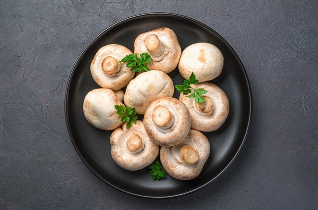 Champignons et persil dans une assiette noire sur fond sombre