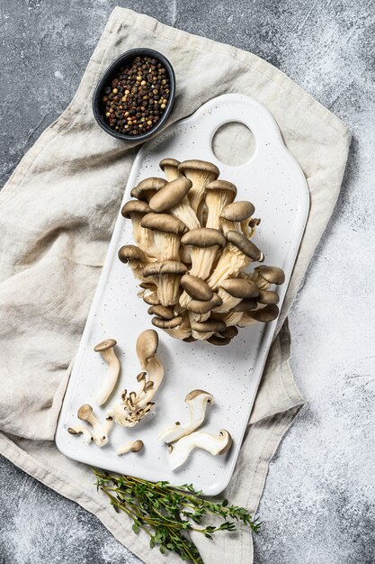 Photo champignons pleurotes sur une planche à découper blanche au thym. fond gris. vue de dessus