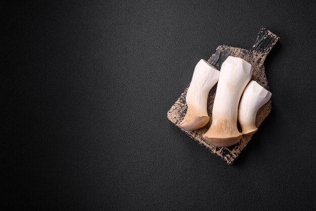Champignons Pleurotus eryngii sur fond de béton foncé Champignons comestibles entiers crus