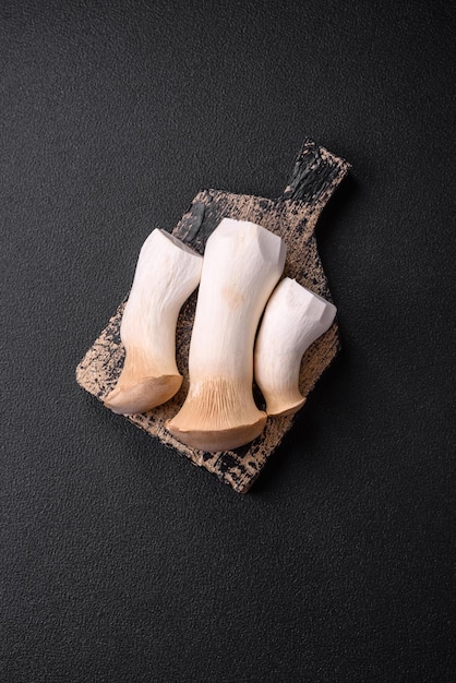 Champignons Pleurotus eryngii sur fond de béton foncé Champignons comestibles entiers crus