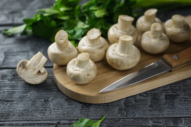 Champignons tranchés frais sur planche à découper et persil sur table en bois foncé