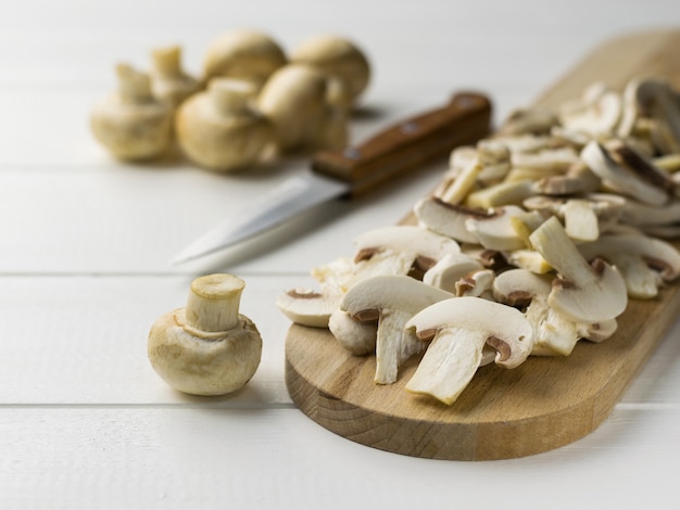 Champignons tranchés frais sur une planche à découper sur une table en bois blanc