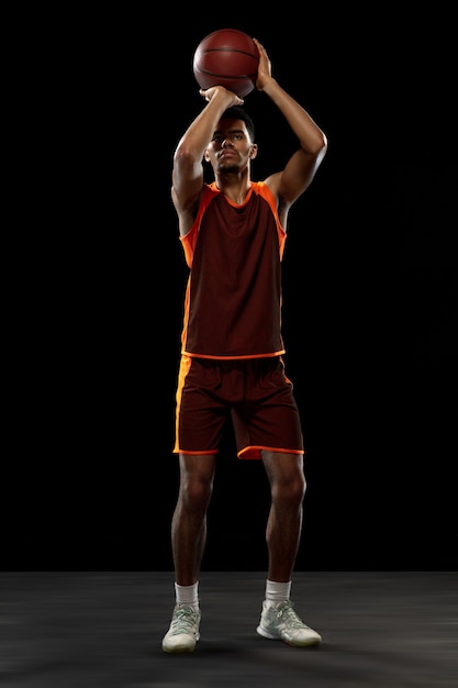 Champion. Jeune joueur de basket-ball afro-américain déterminé, s'entraînant en action, mouvement isolé sur fond noir. Concept de sport, mouvement, énergie et mode de vie sain et dynamique.