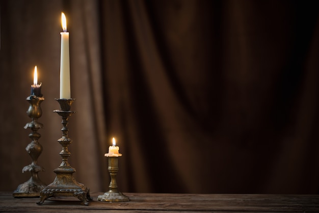 Chandelier antique avec bougie allumée sur la vieille table en bois sur rideau de velours marron