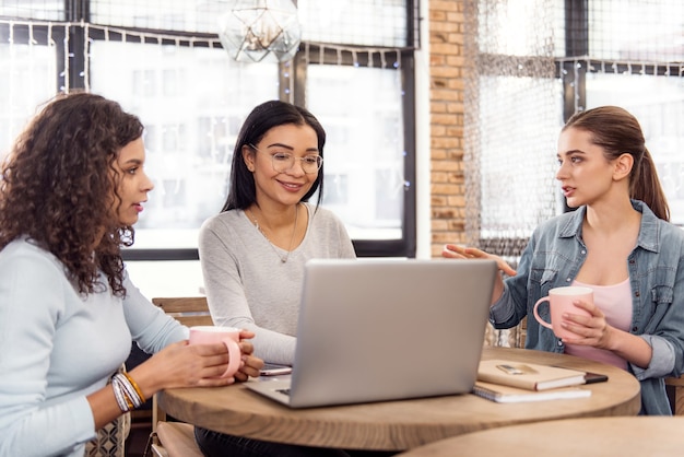 Des changements vitaux. Enthousiaste jolie trois étudiants discutant de présentations tout en sirotant un thé et en posant au café