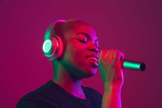 Chanter au casque. Portrait de jeune femme afro-américaine sur fond violet. Beau modèle en chemise noire. Concept d'émotions, expression faciale, ventes, publicité, inclusion, diversité. Espace de copie.