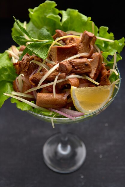 Chanterelles marinées, aux herbes et laitue, dans un bol en verre, sur fond noir