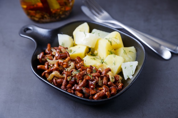 Chanterelles avec pommes de terre bouillies, oignons, aneth et huile dans une petite poêle noire. Plat traditionnel russe