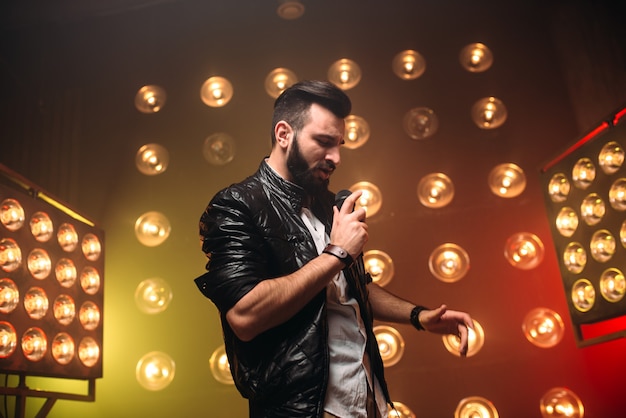 Chanteur barbu brutal avec microphone chanter une chanson sur la scène avec les décorations de lumières