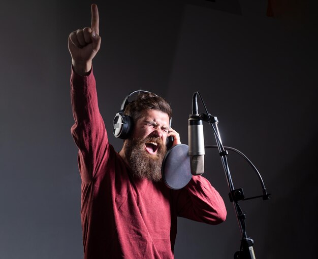 Le chanteur avec un visage d'expression portant des écouteurs interprète une chanson avec un microphone pendant l'enregistrement