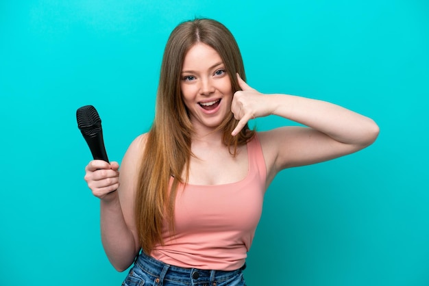 Chanteuse caucasienne femme prenant un microphone isolé sur fond bleu faisant un geste de téléphone rappelez-moi signe