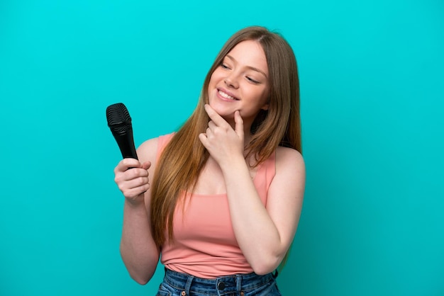 Chanteuse caucasienne femme prenant un microphone isolé sur fond bleu regardant sur le côté et souriant