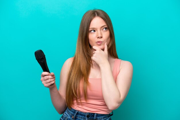 Chanteuse femme caucasienne prenant un microphone isolé sur fond bleu ayant des doutes et pensant