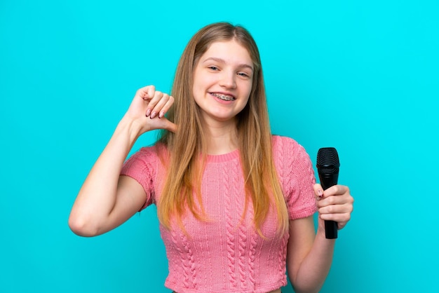 Chanteuse fille russe prenant un microphone isolé sur fond bleu fière et satisfaite