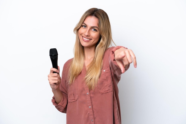 Chanteuse uruguayenne prenant un microphone isolé sur fond blanc pointant vers l'avant avec une expression heureuse