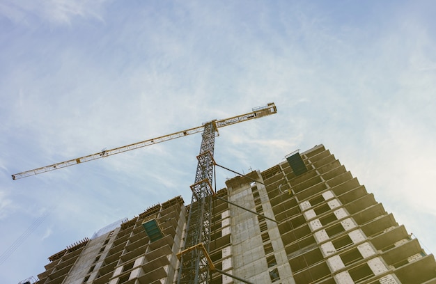 Chantier de construction avec des bâtiments en construction et des maisons résidentielles à plusieurs étages. Grues à tour en action sur fond de ciel bleu
