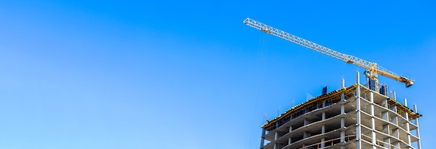Chantier de construction et grande grue jaune sur fond de bannière panoramique de ciel bleu avec photo d'espace de copie