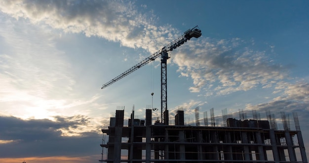 Chantier de construction avec des grues au coucher du soleil jaune orane travaillant avec le téléchargement de métal d'installation élevé