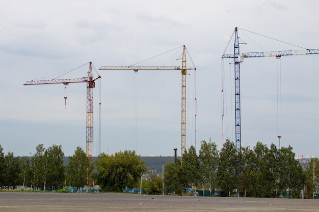 Chantier de construction avec de hautes grues contre le ciel bleu. Un immeuble résidentiel est en construction.