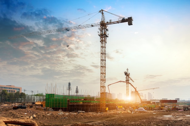 Chantier de construction, silhouettes de travailleurs de l'industrie de la construction sur des échafaudages contre la lumière du coucher du soleil.