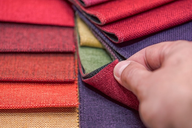 Échantillons de textiles d'ameublement de différentes couleurs et épaisseurs. Détails en gros plan d'échantillons de texture de tissu multicolore. Un homme prélève un échantillon de tissu et en vérifie la qualité au toucher.