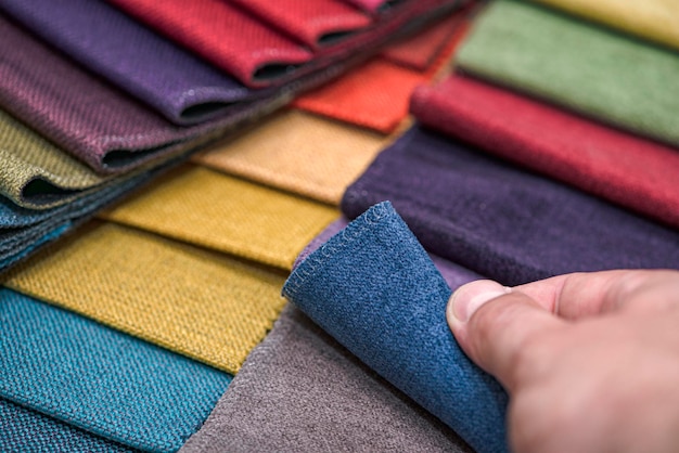 Échantillons de textiles d'ameublement de différentes couleurs et épaisseurs. Détails en gros plan d'échantillons de texture de tissu multicolore. Un homme prélève un échantillon de tissu et en vérifie la qualité au toucher.