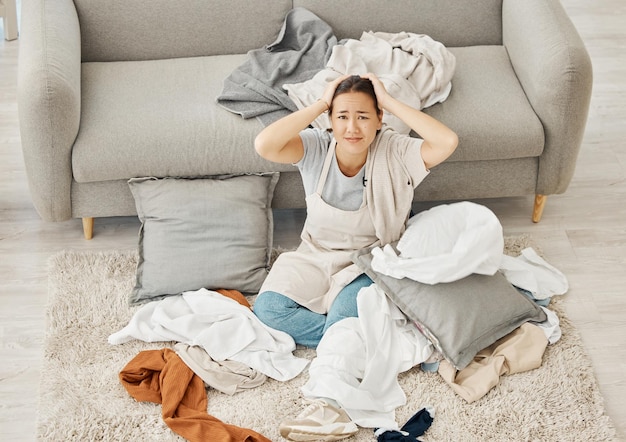 Chaos de lessive stress de nettoyage et femme fatiguée d'anxiété sur le sol du salon épuisement confus et triste dans le salon de l'appartement avec des vêtements Portrait de nettoyeur de service avec problème de désordre à la maison