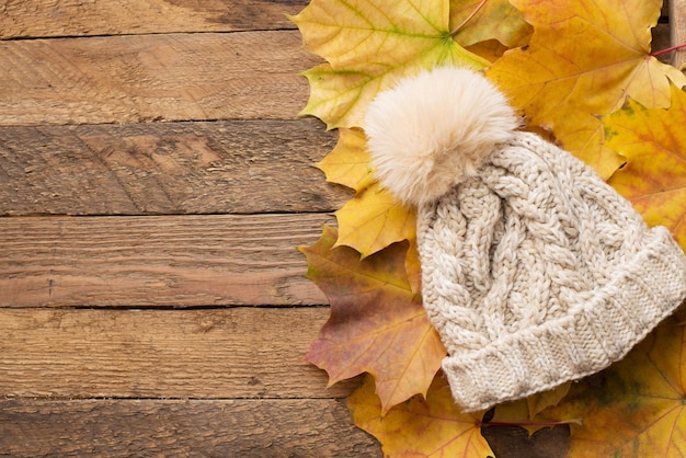 Un chapeau d'automne chaud avec des feuilles d'hiver sur un tissu de bois