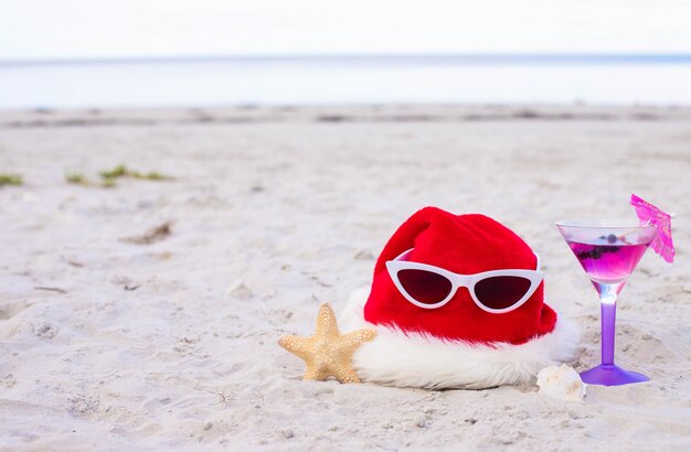 Photo le chapeau du père noël sur la plage avec un cocktail d'étoile de mer et des lunettes de soleil