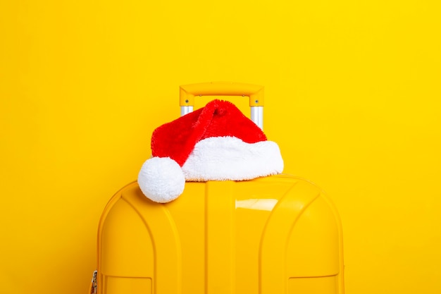 Le chapeau du Père Noël repose sur une valise jaune sur fond jaune.