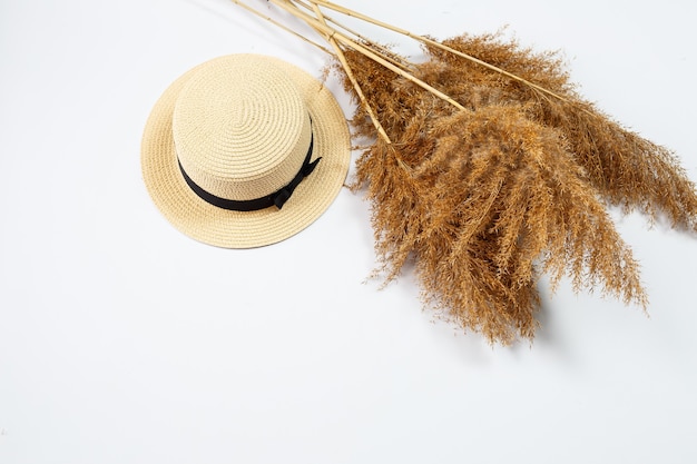 Chapeau d'été féminin et herbe sèche sur fond blanc. Vacances d'été, vacances, voyage, concept de voyage. Vue de dessus des accessoires de plage. Espace pour le texte.