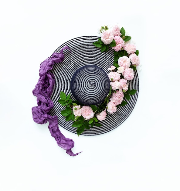 Chapeau d'été avec un motif de roses roses naturelles fraîches et une écharpe violette en soie légère sur fond blanc.