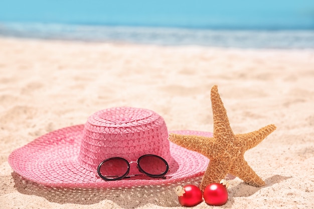 Chapeau avec étoile de mer, décorations et lunettes de soleil sur la plage. Notion de vacances de Noël