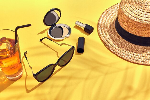 Chapeau de femme de plage de paille, boisson avec de la glace dans un verre et lunettes de soleil sur fond jaune